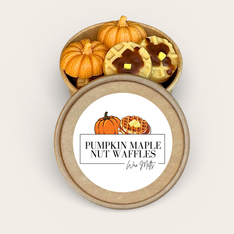 A round kraft paper gift box shown open, with miniature pumpkin-shaped items and nut-waffle shaped wax melts inside. The lid is placed in front and features a white label with the text 'PUMPKIN MAPLE NUT WAFFLES'.