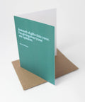 A teal greeting card with white text reading 'Instead of gifts this year, I'm giving everyone my opinion.' and 'Merry Christmas,' shown standing upright with a brown kraft envelope behind it on a white background.