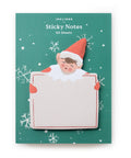 sticky note pad shaped like holiday elf holding large card. elf is dressed in red on green background board