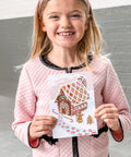girl holding gingerbread house holiday card with candy looking stickers for decorating the gingerbread house