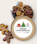 Open round kraft gift box filled with gingerbread-shaped cookie wax melts, with two additional gingerbread cookie wax melts placed beside it on a light beige background. The lid label reads “SPICED GINGERBREAD” with a small holiday illustration.