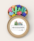 A round kraft paper gift box shown open, filled with colorful sculpted succulents and cacti wax melts. The lid is placed in front and features a white label with a watercolor cactus illustration and the text 'SUCCULENTS'.