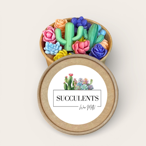 A round kraft paper gift box shown open, filled with colorful sculpted succulents and cacti wax melts. The lid is placed in front and features a white label with a watercolor cactus illustration and the text 'SUCCULENTS'.