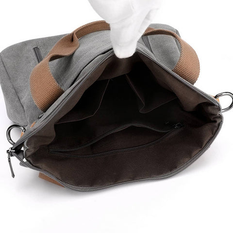 An open gray and brown canvas bag with a white-gloved hand lifting the top flap to show the interior compartments, photographed on a white background.