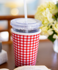 Red and white checkered coffee sleeve around a cup with straw on a blurred background