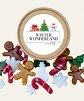 A round kraft paper gift box labeled 'WINTER WONDERLAND' with illustrated holiday graphics, surrounded by assorted gingerbread-themed and Christmas-shaped soaps on a light beige background.