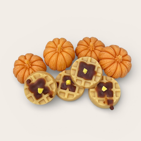 A set of miniature autumn-themed craft wax melts featuring five small orange pumpkins and five round waffle cookies topped with dark brown syrup and yellow butter details, arranged on a light beige background.