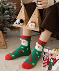 Person wearing festive socks with animal designs, holding small triangular gift boxes, Christmas tree in the background.