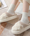 White fuzzy slippers worn with light gray socks on a patterned floor.