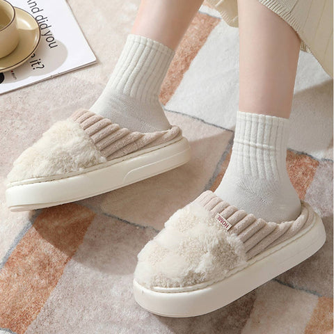 White fuzzy slippers worn with light gray socks on a patterned floor.