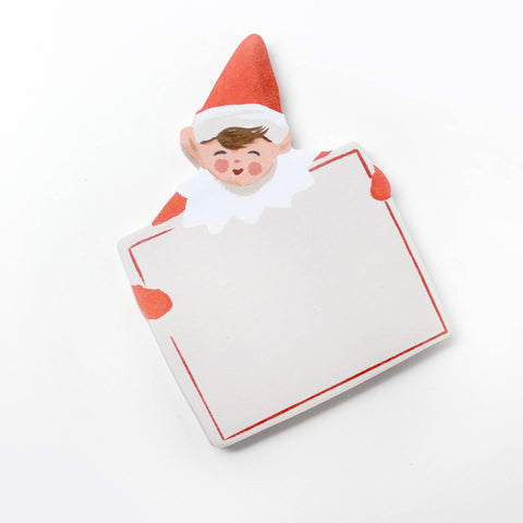 sticky note pad shaped like holiday elf holding large card. elf is dressed in red on green background board