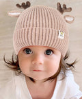 Child wearing a beige knit hat with reindeer antlers on a neutral background