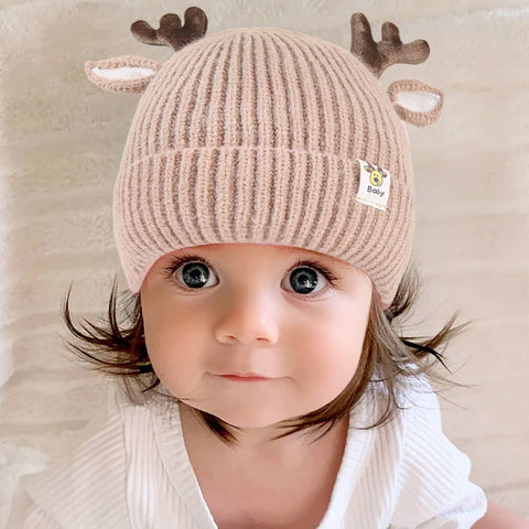 Child wearing a beige knit hat with reindeer antlers on a neutral background