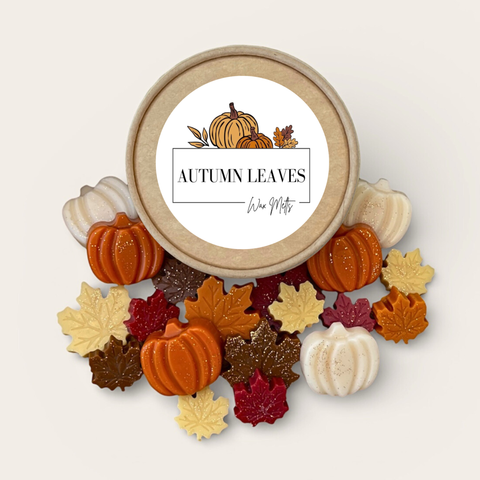 assorted fall wax melts in various shapes like leaves and pumpkins sprinkled on a white background surrounding their kraft colored container
