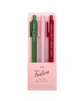 A boxed set of three festive gel pens in green, light pink, and dark red, displayed in a light pink window box. The pens feature white text reading 'THINSEL & TINS', 'NICE LUST ENERGY', and 'HAPPY MERRY EVERYTHING!'.