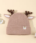 Beige knit baby hat with reindeer antlers and ears on a beige background