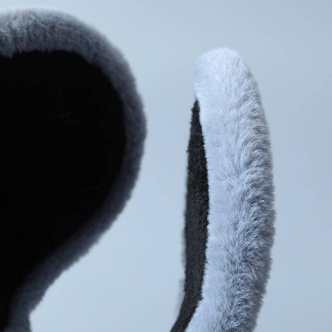 Close-up of a plush faux-fur ear warmer with a dark charcoal interior and a light gray outer edge, shown against a pale blue-gray background.
