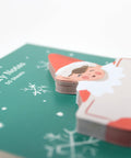 sticky note pad shaped like holiday elf holding large card. elf is dressed in red on green background board