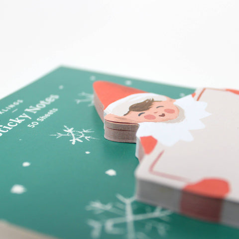 sticky note pad shaped like holiday elf holding large card. elf is dressed in red on green background board