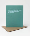 A teal greeting card with white text reading, 'Instead of gifts this year, I'm giving everyone my opinion.' and 'Merry Christmas,' standing upright on a brown kraft envelope against a light gray background.
