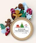 A round kraft gift tin filled with assorted Christmas-themed wax melts, shown open with several pieces spilled beside it. The lid features a white label with the text 'WINTER WONDERLAND' and small holiday illustrations including a Christmas tree, snowman, and candy cane.