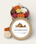 An open round kraft paper gift box filled with decorative autumn-themed wax melts, with the lid placed in front. The wax melts are shaped like pumpkins, leaves, and small white pumpkins.