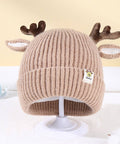 Beige knit baby hat with reindeer antlers on a white stand against a light background