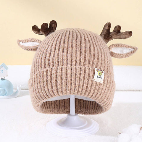 Beige knit baby hat with reindeer antlers on a white stand against a light background