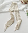 Beige striped scarf on a white surface with a magazine and cup in the background