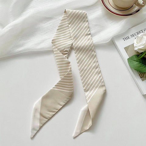 Beige striped scarf on a white surface with a magazine and cup in the background