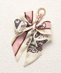 Decorative keychain with a bow made from a cream and brown patterned fabric on a textured white background