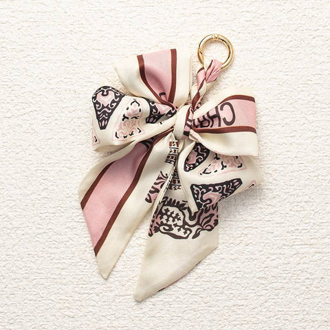 Decorative keychain with a bow made from a cream and brown patterned fabric on a textured white background
